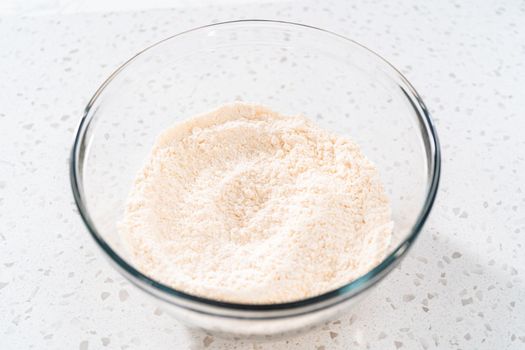 Mixing dry ingredients with a hand whisk in a large glass mixing bowl to bake a simple vanilla bundt cake.