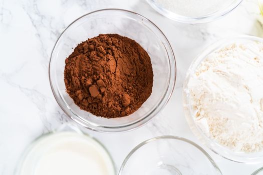 Measured ingredients in glass mixing bowls to prepare chocolate cupcake.