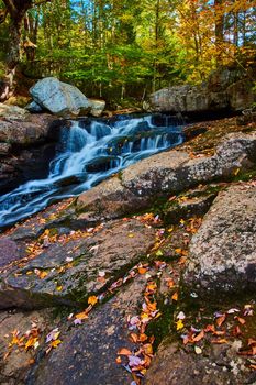 Image of Forest with cascading river waterfalls small along rocky edge covered in fall leaves