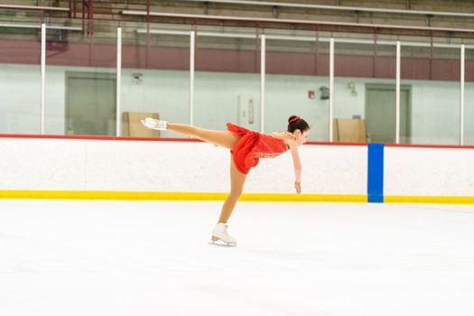 Teenage girl practicing figure skating on an indoor ice skating rink.