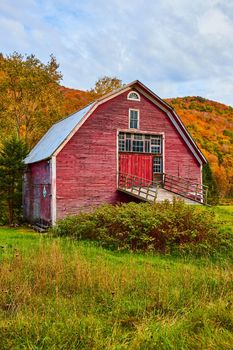 Image of Up close to beautiful red barn aging in fields with colorful fall mountains behind