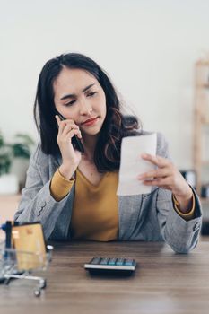 Young Asian Woman checking bills, bank account balance, taxes and calculating expenses at home.