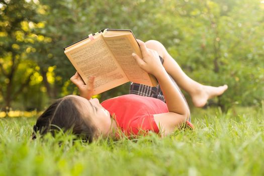 Adorable cute little girl reading book outside on grass.