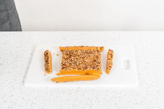 Cutting pumpkin spice fudge into square pieces on a white cutting board.