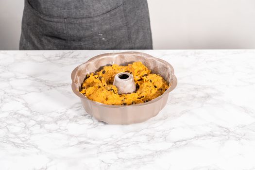 Pouring cake batter into a greased bunt cake pan to bake chocolate pumpkin bundt cake with toffee glaze.