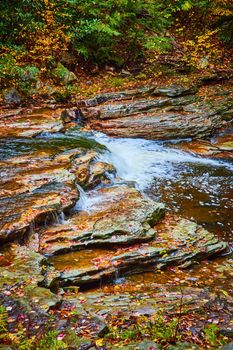 Image of Waterfall small cascading through creek with fall leaves covering fall rocks