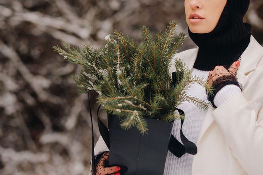 A girl in a white suit and balaclava with a package of Christmas trees in the winter forest on New Year's Eve.New Year's concept.