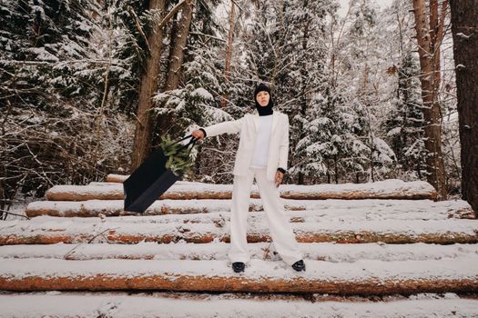 A girl in a white suit and balaclava with a package of Christmas trees in the winter forest on New Year's Eve.New Year's concept.