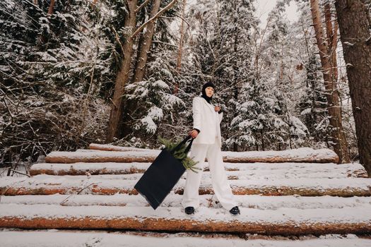 A girl in a white suit and balaclava with a package of Christmas trees in the winter forest on New Year's Eve.New Year's concept.