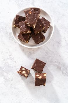 Homemade chocolate macadamia fudge square pieces on a white plate.