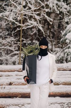 A girl in a white suit and balaclava with a package of Christmas trees in the winter forest on New Year's Eve.New Year's concept.