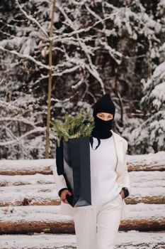 A girl in a white suit and balaclava with a package of Christmas trees in the winter forest on New Year's Eve.New Year's concept.