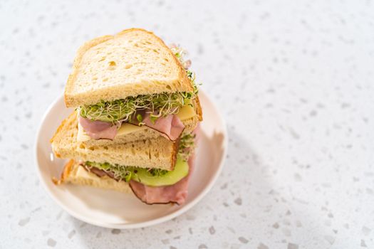 Stack of ham, cucumber, and sprout sandwiches on the white plate