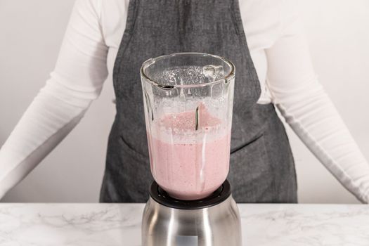 Blending ingredients for healthy breakfast strawberry banana smoothie in a kitchen blender.