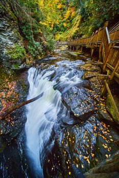 Image of Boardwalk along river with raging falls into abyss and cliffs covered in golden fall leaves
