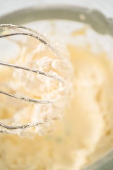Mixing ingredients in a large glass mixing bowl of kitchen mixer to make eggnog buttercream frosting.