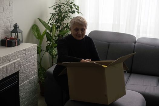 Elderly woman unpacking things in new house. opening cardboard box. Real estate, purchase concept.