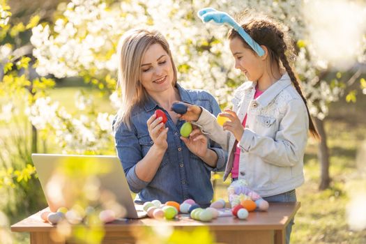 Mother and her daughter painting eggs. Happy family preparing for Easter. Cute little child girl wearing bunny ears.