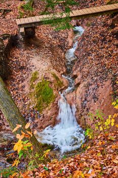 Image of Clay carved river creek with waterfall and walking bridge in fall forest