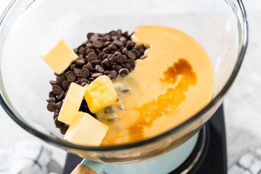 Melting white chocolate chips and other ingredients in a glass mixing bowl over boiling water to prepare chocolate macadamia fudge.