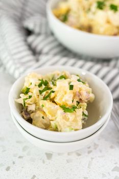 Serving potato salad garnished with fresh parsley in a white ceramic bowl.