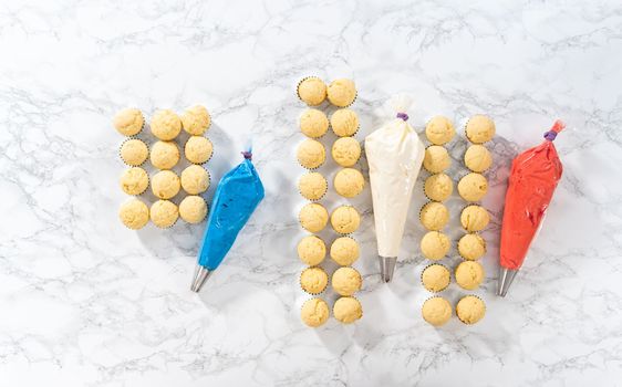 Flat lay. Frosting mini vanilla cupcakes with buttercream frosting to make an American flag mini cupcake cake.