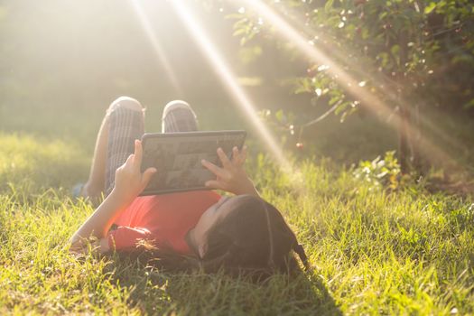 Child girl playing on a Digital tablet in the garden. Online or Remote education concept.