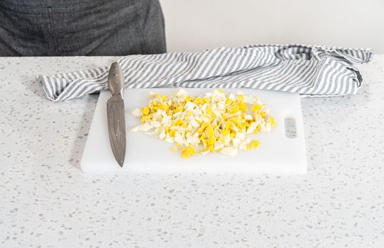 Cutting hard-boiled eggs on a white cutting board to make potato salad.