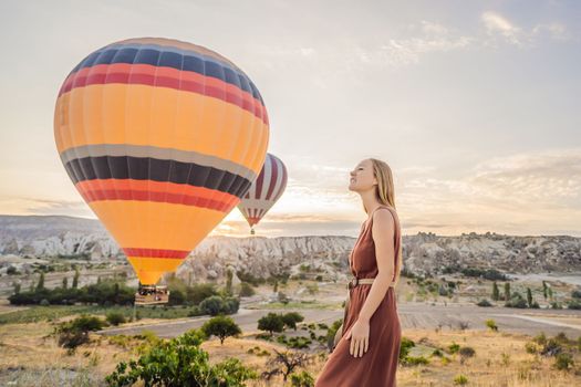 Tourist woman looking at hot air balloons in Cappadocia, Turkey. Happy Travel in Turkey concept. Woman on a mountain top enjoying wonderful view.