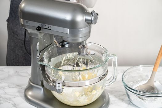 Mixing ingredients in a large glass mixing bowl of kitchen mixer to make eggnog buttercream frosting.