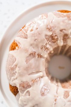 Freshly baked simple vanilla bundt cake with a white glaze on a serving plate.