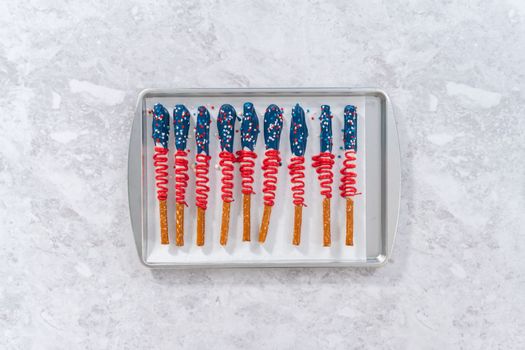 Flat lay. Homemade chocolate-covered pretzel rods decorated like the American flag drying on a baking sheet lined with parchment paper.