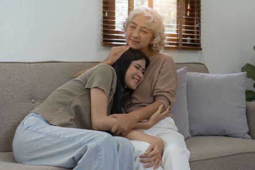 Loving adult daughter hugging older mother on couch at home, family enjoying tender moment together, young woman and mature mum or grandmother looking at each other, two generations.