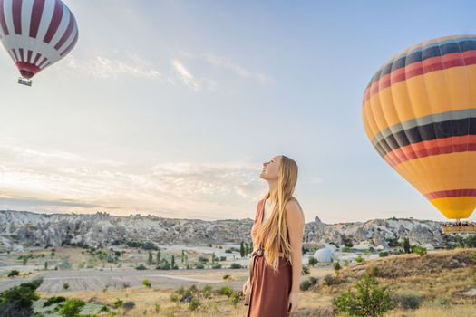 Tourist woman looking at hot air balloons in Cappadocia, Turkey. Happy Travel in Turkey concept. Woman on a mountain top enjoying wonderful view.