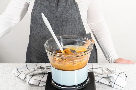 Melting chocolate chips and other ingredients in a glass mixing bowl over boiling water to prepare pumpkin spice fudge.