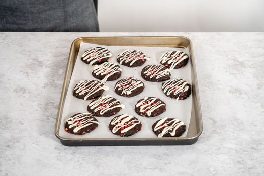 Drizzling melted white chocolate over freshly baked chocolate cookies with peppermint chips.