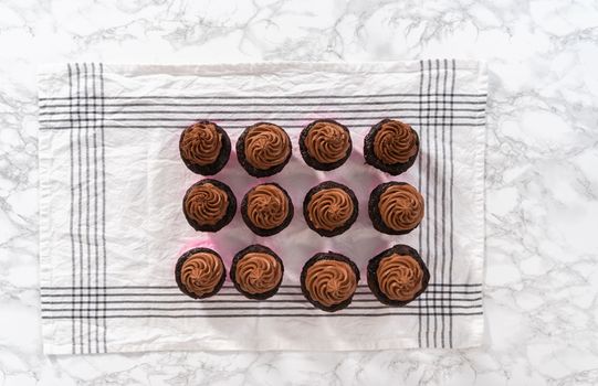 Flat lay. Piping chocolate ganache frosting on top of chocolate cupcakes.