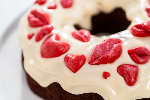 Freshly baked red velvet bundt cake with chocolate lips and hearts over cream cheese glaze for Valentine's Day.