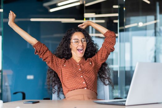 Tired businesswoman in office stretching and yawning, latin american woman indoors working at workplace using laptop bored overtired.