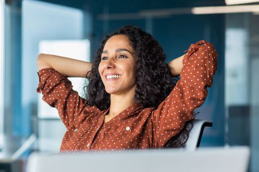 Happy and smiling successful hispanic business woman finished work satisfied with work result and achievement, hands behind head and smiling close up.