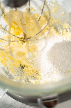 Mixing ingredients in a large glass mixing bowl of kitchen mixer to make eggnog buttercream frosting.