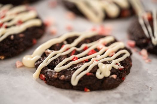 Freshly baked chocolate cookies with peppermint chips with a white chocolate drizzle on top.