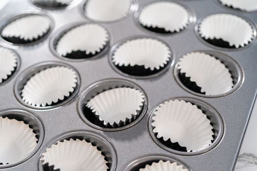 Scooping cupcake batter with dough scoop into a baking pan with liners to bake American flag mini cupcakes.