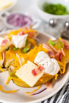 Pressure Cooker Baked Potatoes. Garnished large baked potatoes with butter, sour cream, cheese, and bacon bits on a white plate.