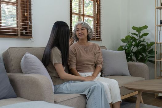Loving adult daughter hugging older mother on couch at home, family enjoying tender moment together, young woman and mature mum or grandmother looking at each other, two generations.