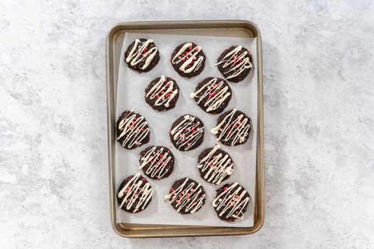 Flat lay. Drizzling melted white chocolate over freshly baked chocolate cookies with peppermint chips.
