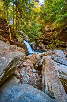 Image of Large boulders near stunning waterfall with blue waters and cliffs covered in fall trees