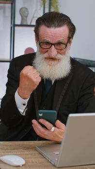 Oh my God, Wow. Happy amazed senior old businessman working on smartphone shocked by sudden victory, game winning, lottery jackpot achievemen, good news. Elderly manager man freelancer at home office