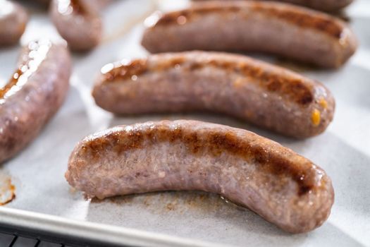 Freshly cooked in oven beer bratwursts on a baking sheet lined with parchment paper.