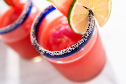Frozen watermelon margarita in a glass garnished with salt, a slice of fresh watermelon, and lime.